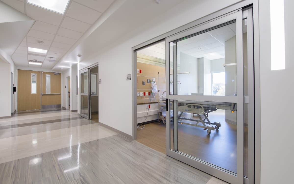 A hallway in a hospital with sliding glass doors.