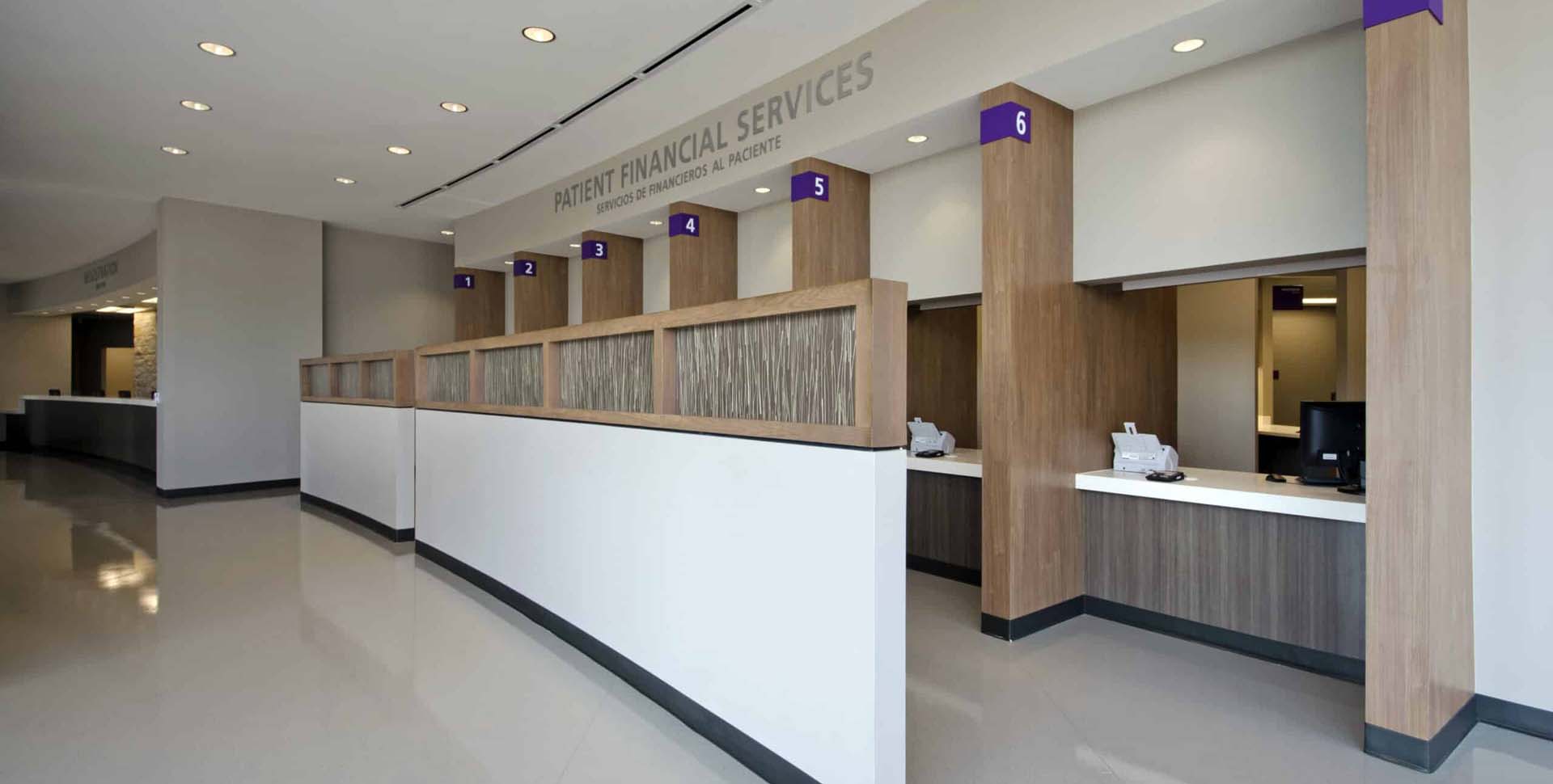 A row of numbered service windows in a modern patient financial services office, with wood accents and computers on the counters.