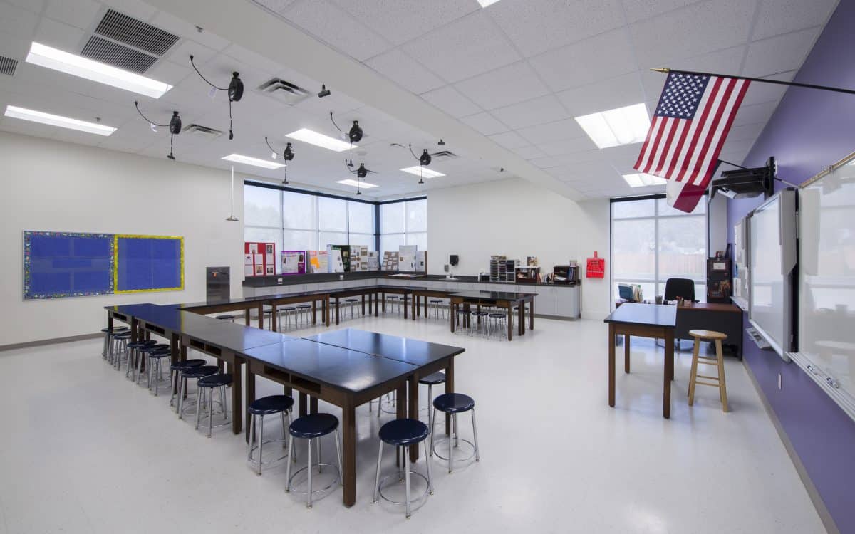 A classroom with tables and chairs and an american flag.