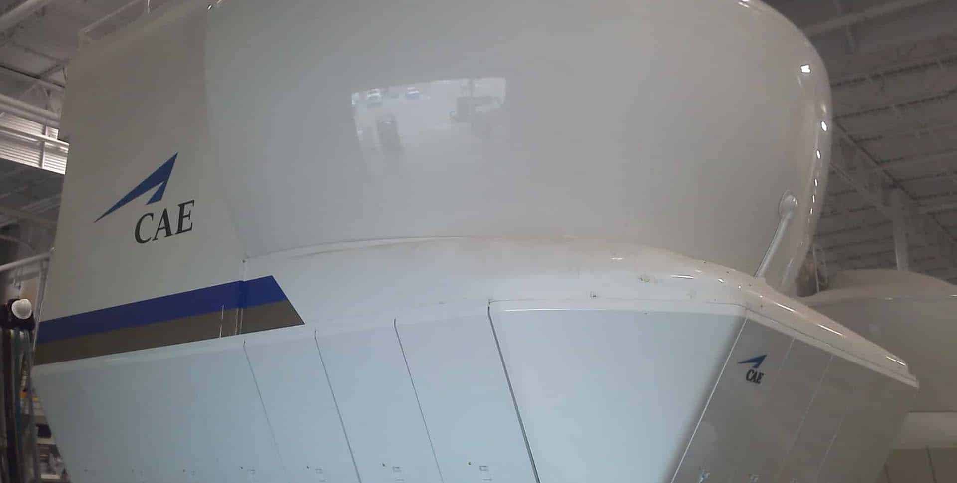 CAE aircraft flight simulator inside a training facility, showing the exterior structure with the CAE logo visible.