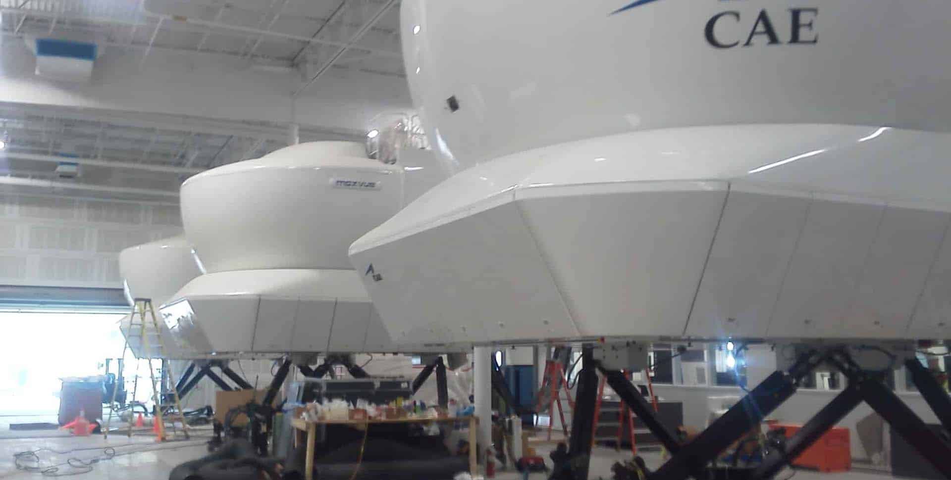 Several full-flight simulators are lined up in a large indoor facility, with maintenance equipment and workstations visible nearby.