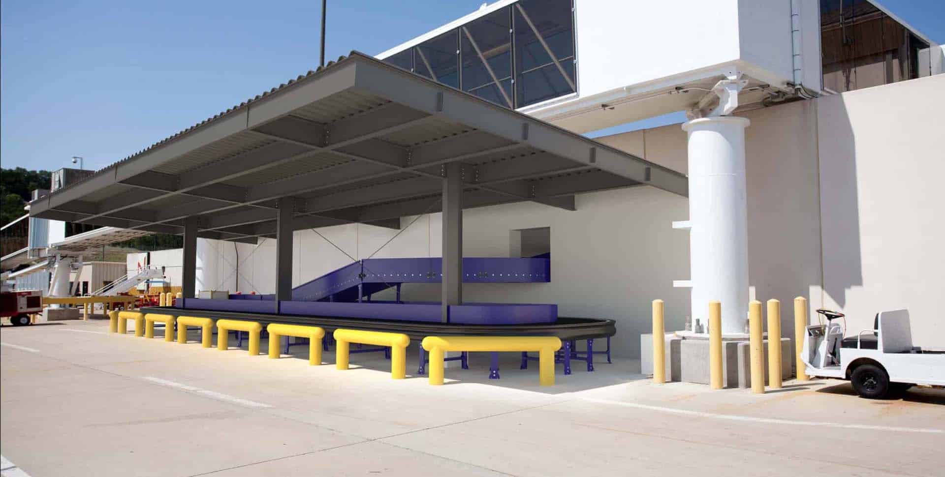 Outdoor baggage conveyor area at an airport with yellow rails, a purple conveyor belt system, and nearby protective bollards.