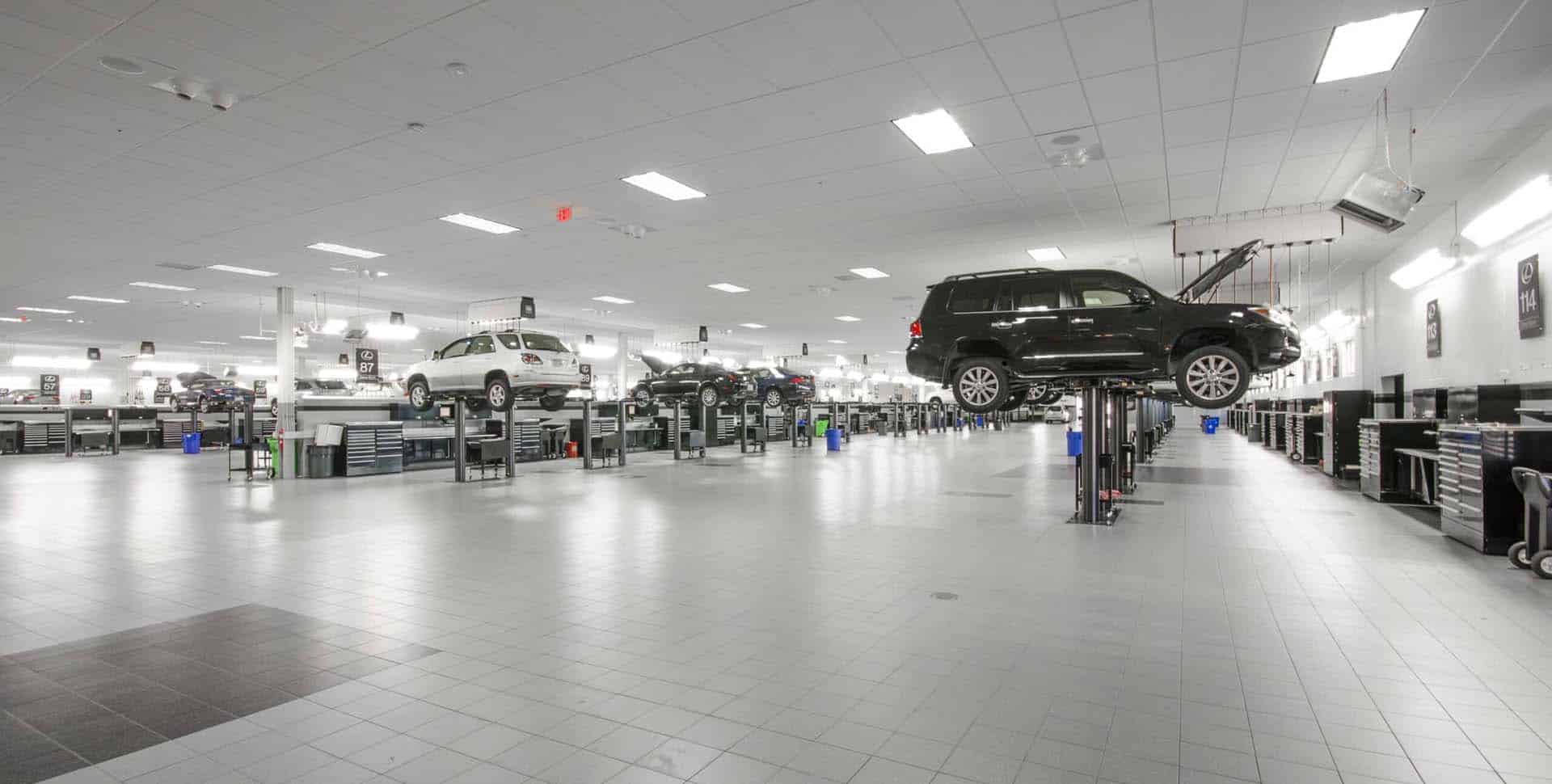 A spacious, brightly lit auto repair shop with vehicles raised on hydraulic lifts and multiple workstations lining the walls.