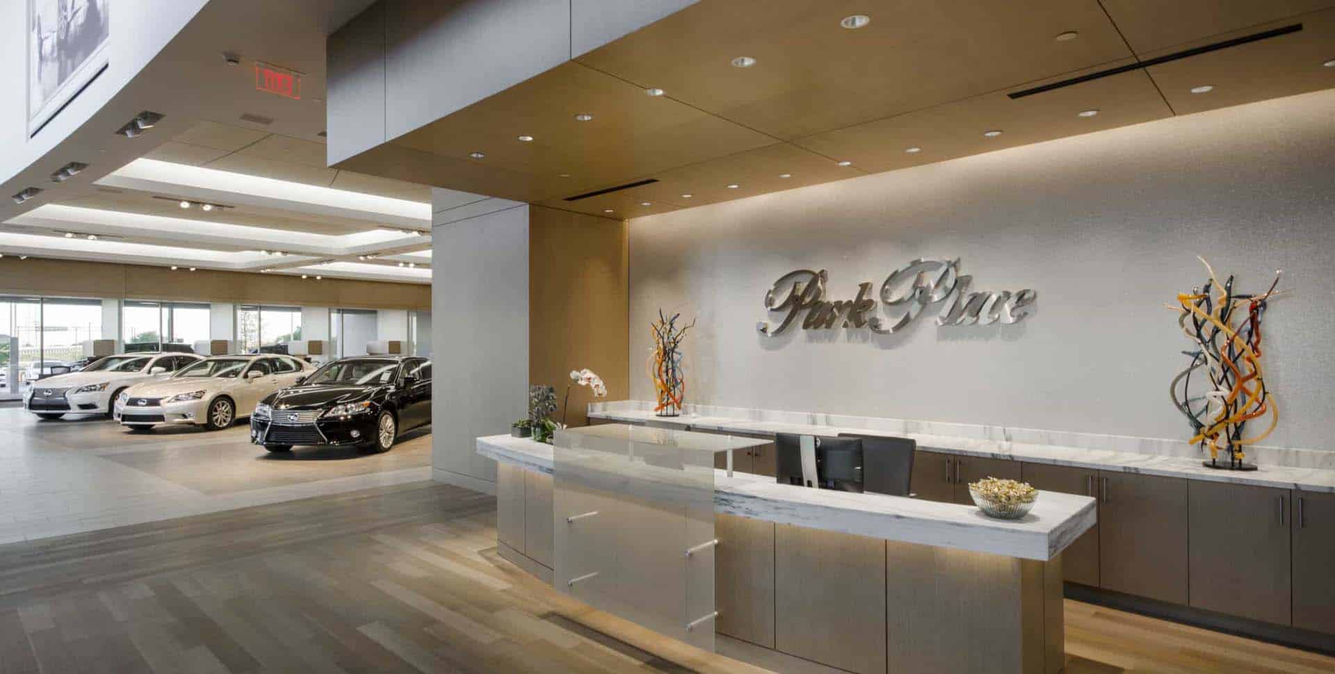 Modern car dealership showroom with a reception desk in the foreground and several cars displayed in the background.