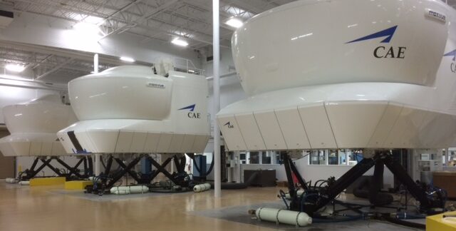 Several full-flight simulators are lined up in a large indoor facility.