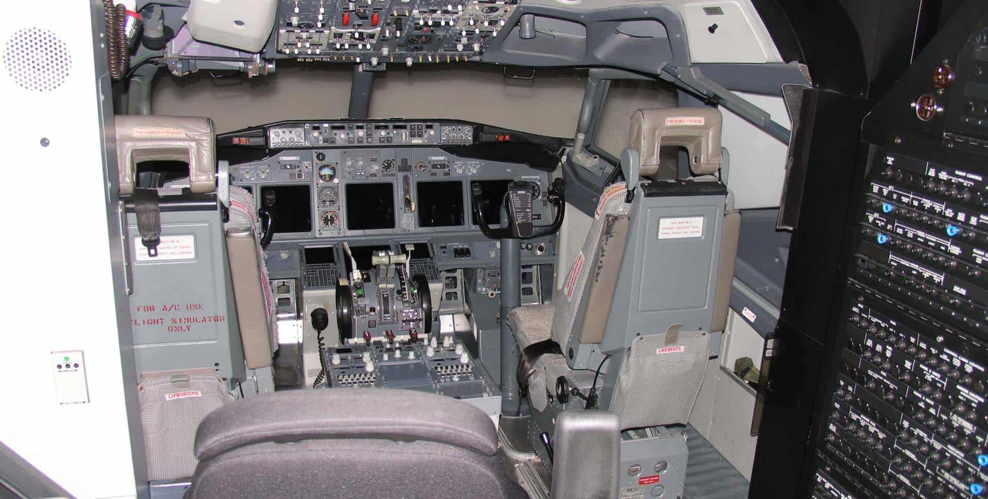 Cockpit of a commercial airplane featuring control panels, multiple screens, switches, and two pilot seats.