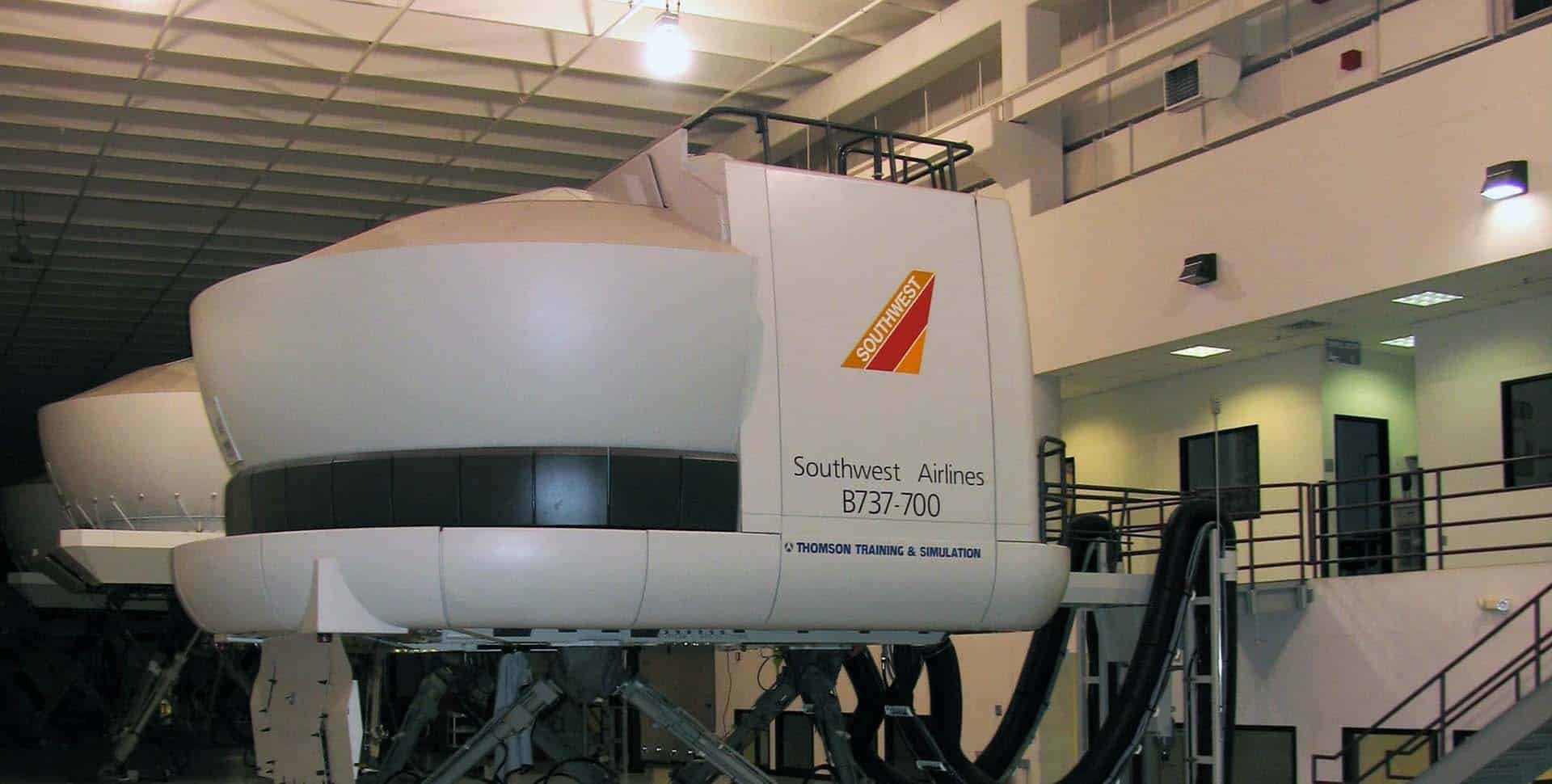 Flight simulator labeled "Southwest Airlines B737-700" inside a training facility with elevated walkways and bright overhead lighting.