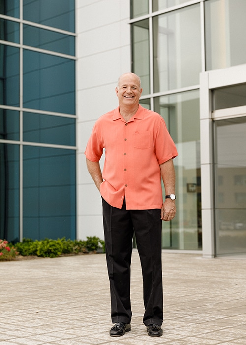 A man in an orange shirt standing in front of a building.