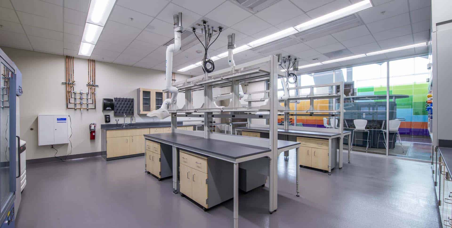 Modern laboratory with empty workbenches, chairs on racks, storage cabinets, equipment, and large windows letting in natural light.