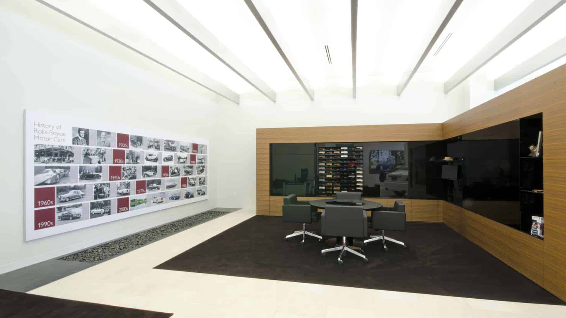 Modern showroom interior with a timeline display on the wall, a round table with four chairs, and a wall-mounted car model collection.