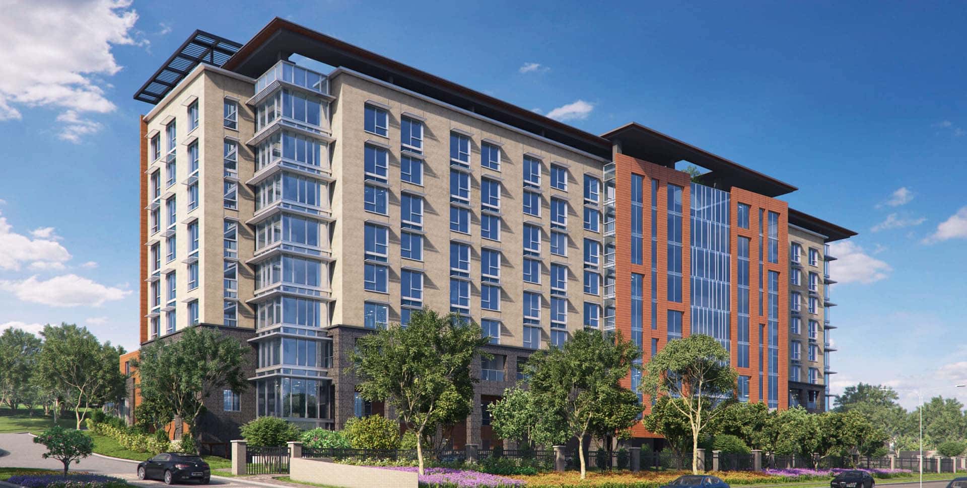 A modern mid-rise apartment building with large windows, surrounded by trees and landscaping, under a clear blue sky.