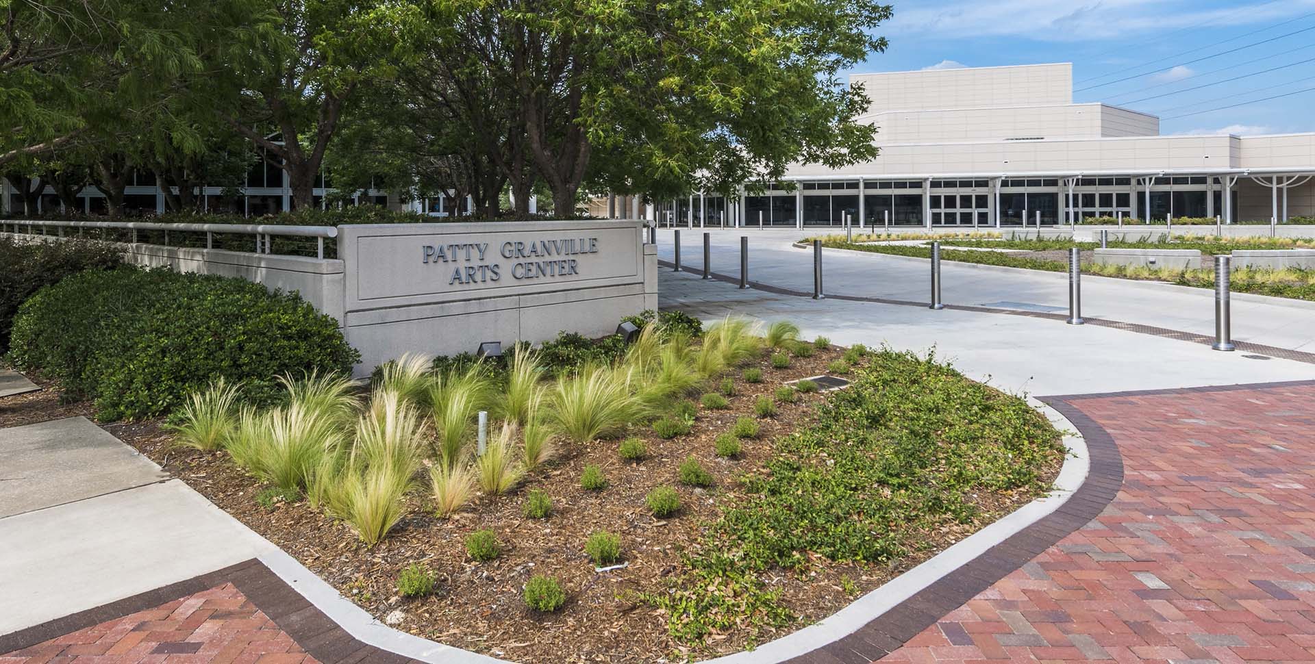 Patty Granville Arts Center sign in front of a landscaped garden area, with a modern building and paved walkway in the background.