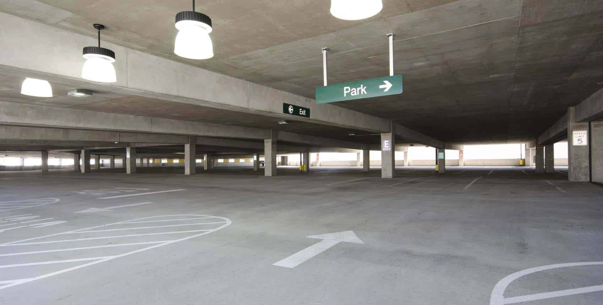 Empty multi-level parking garage with overhead lights, directional arrows, and a green sign indicating "Park" with an arrow to the right.