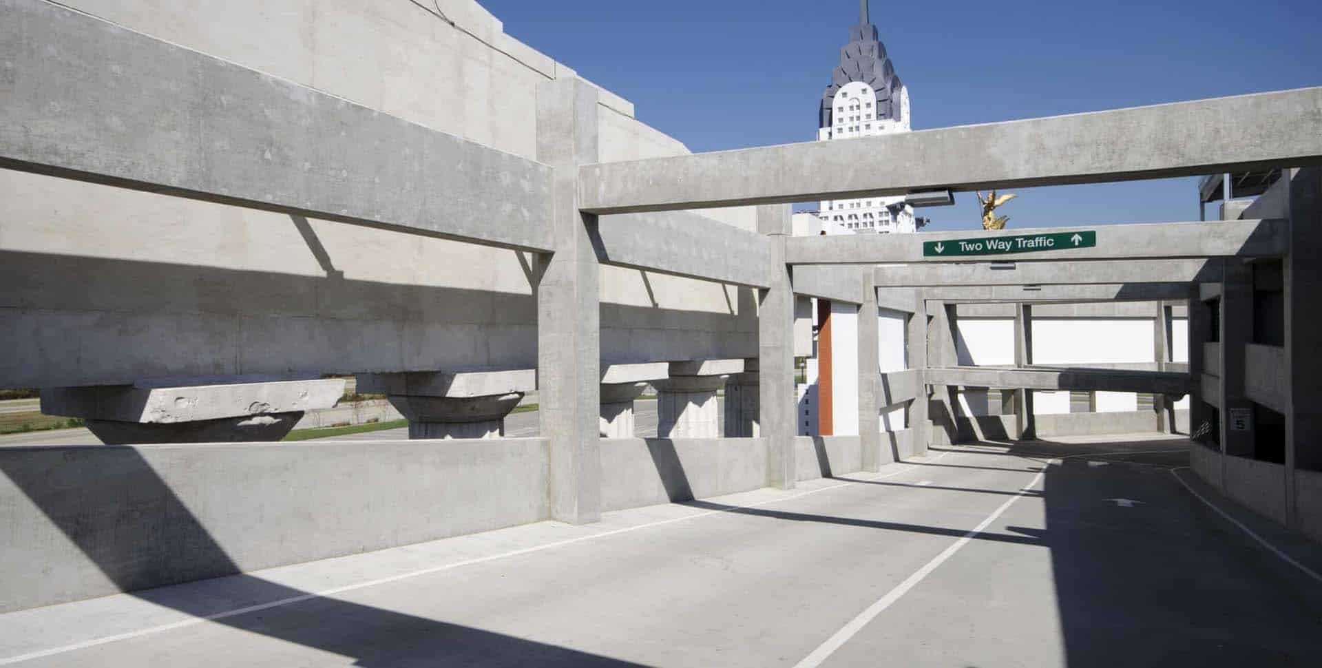A concrete parking garage with a "Two Way Traffic" sign; buildings are visible in the background under a clear blue sky.