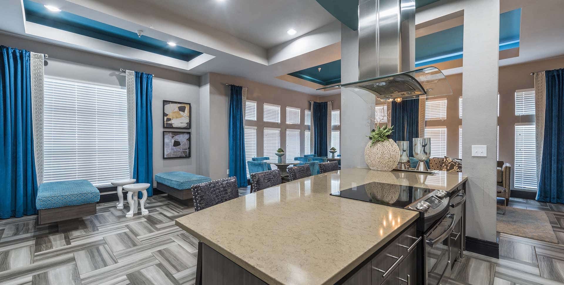 Modern open-concept kitchen and living area with quartz countertops, teal accents, large windows with blue curtains, and patterned tile flooring.