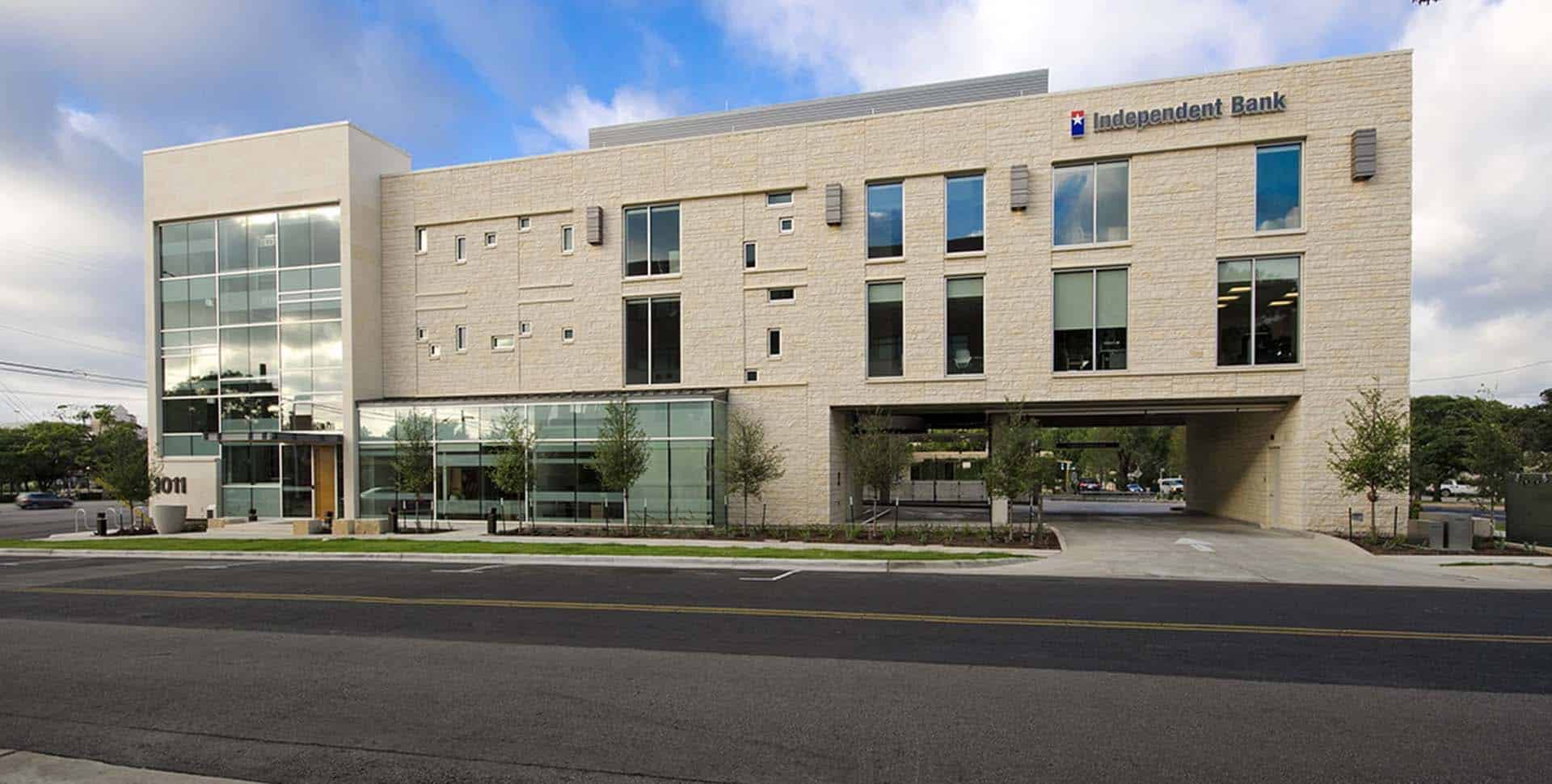 A modern three-story building with large windows and a sign reading "Independent Bank" on the facade, situated along a street with a few small trees in front.
