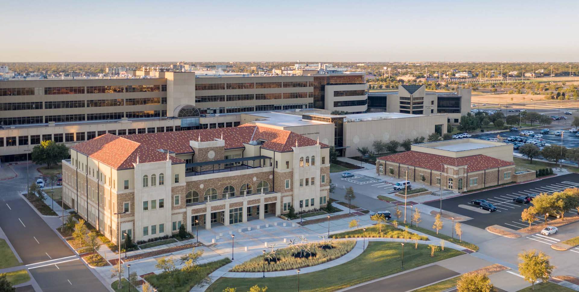 A large medical complex with multiple buildings, red-tiled roofs, and parking areas, viewed from above on a clear day.