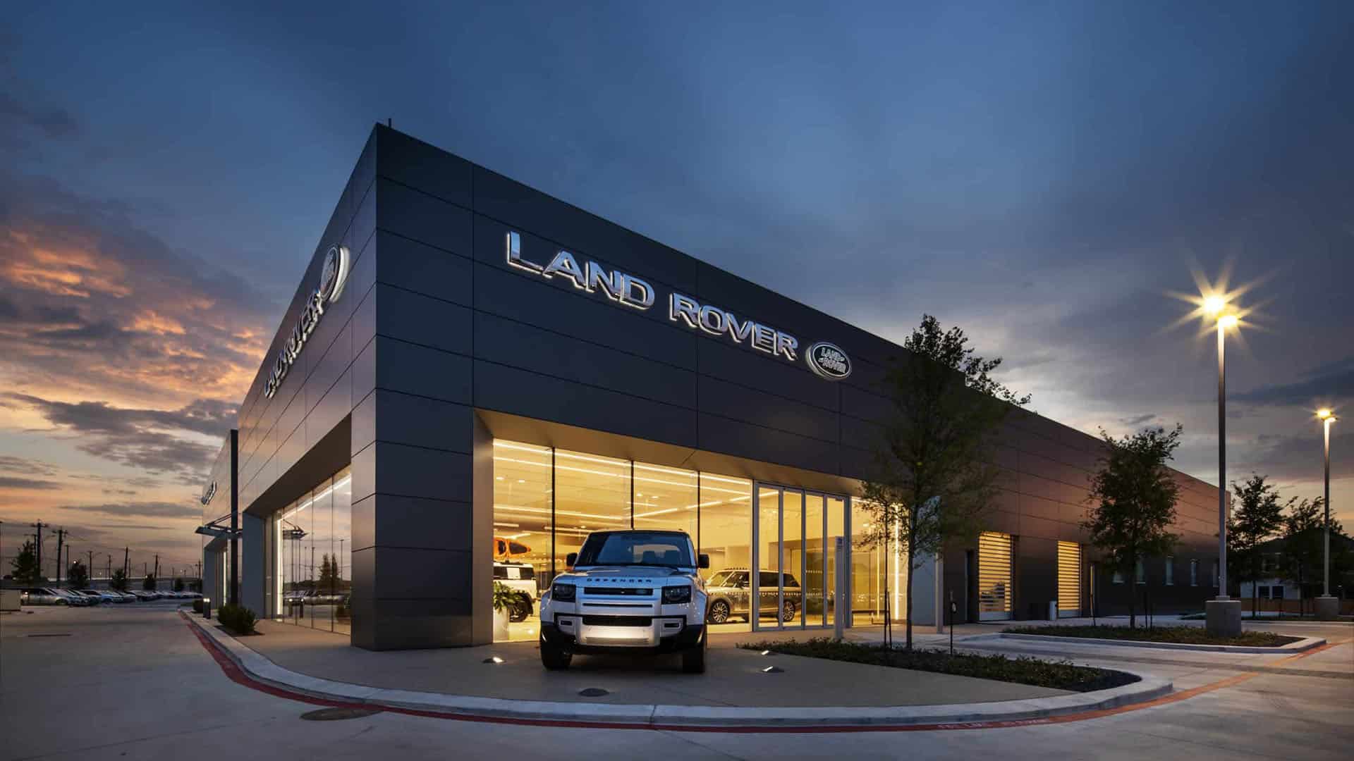 Modern Land Rover dealership building at dusk with illuminated windows and a white Land Rover SUV parked in front.