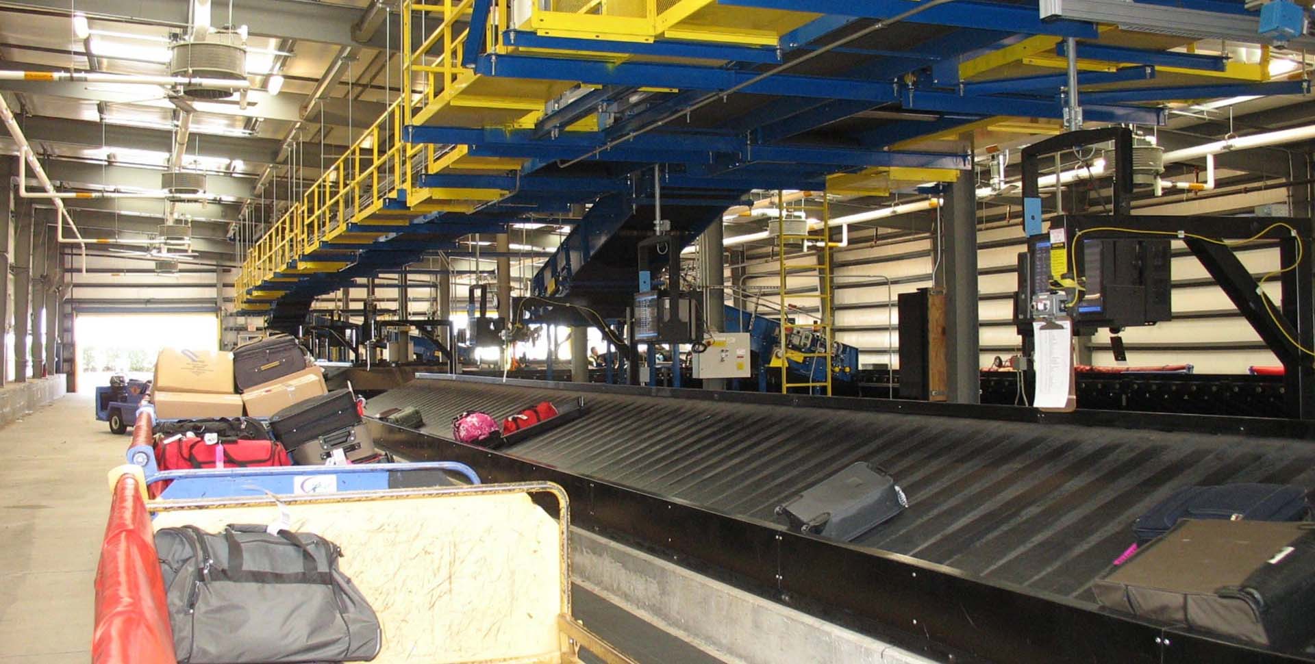 Baggage conveyor system inside an airport facility with suitcases and bags moving along the conveyor belt.