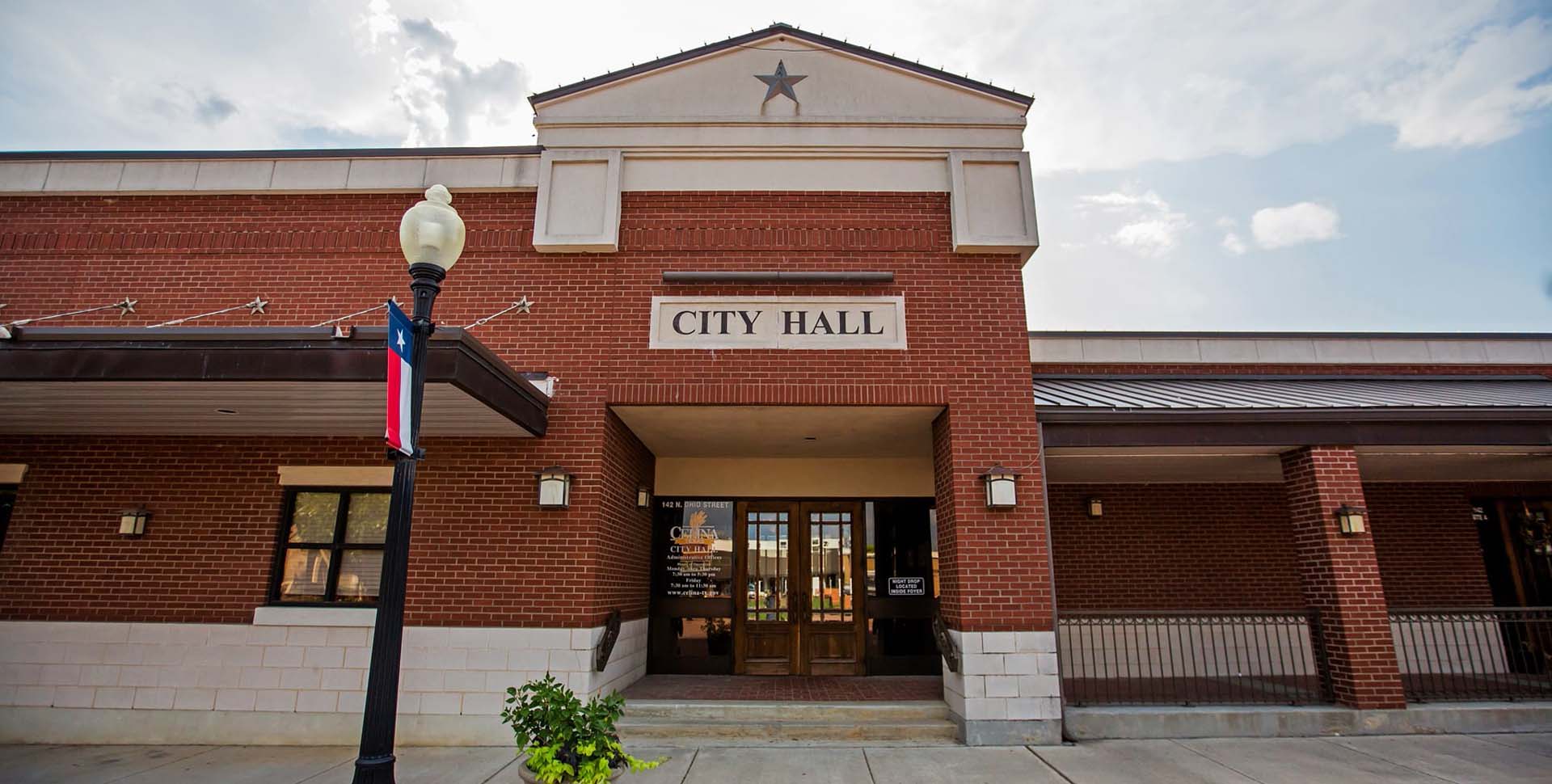 A brick building with a sign reading "City Hall" above the entrance, a star on the facade, and a street lamp in front.