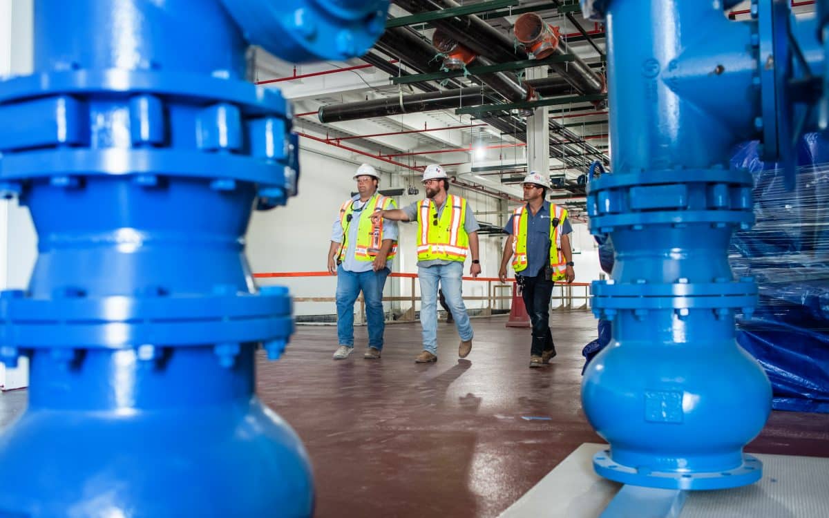 Three construction workers standing in front of blue valves.