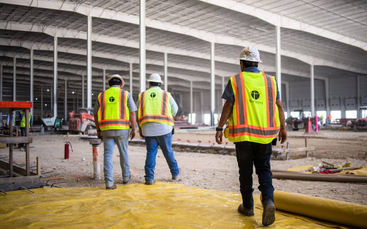 Three construction workers walking through a warehouse.