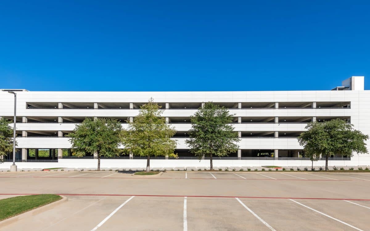 A white building with a parking lot and trees.