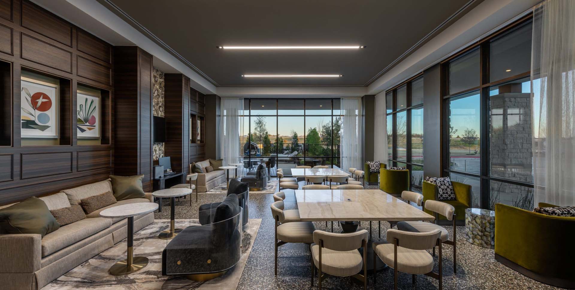Modern lounge area with tables, chairs, sofas, large windows, and wall art, featuring neutral colors and contemporary decor.