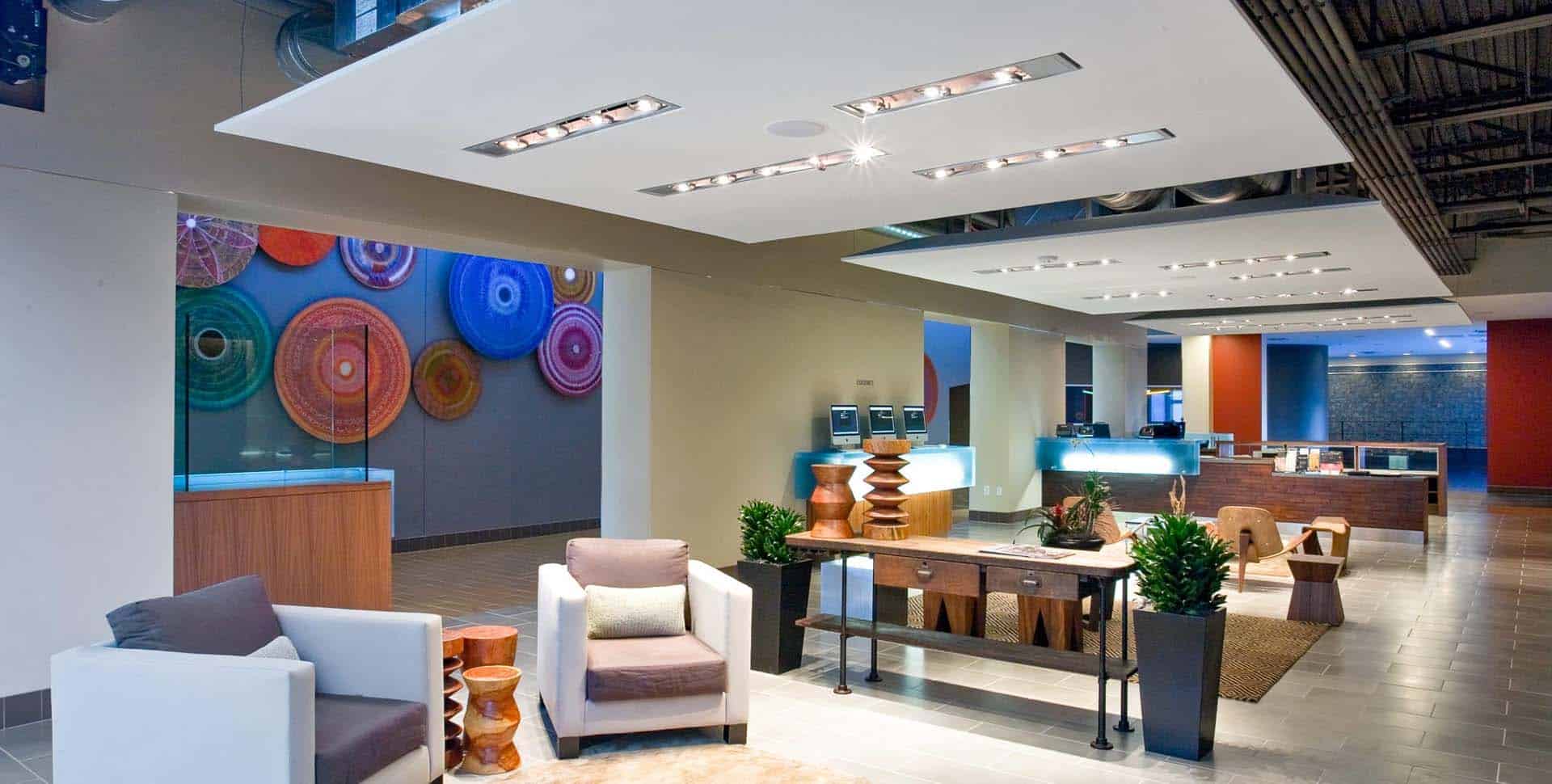 Modern office lobby with contemporary furniture, wooden decor pieces, potted plants, and colorful circular wall art in the background.