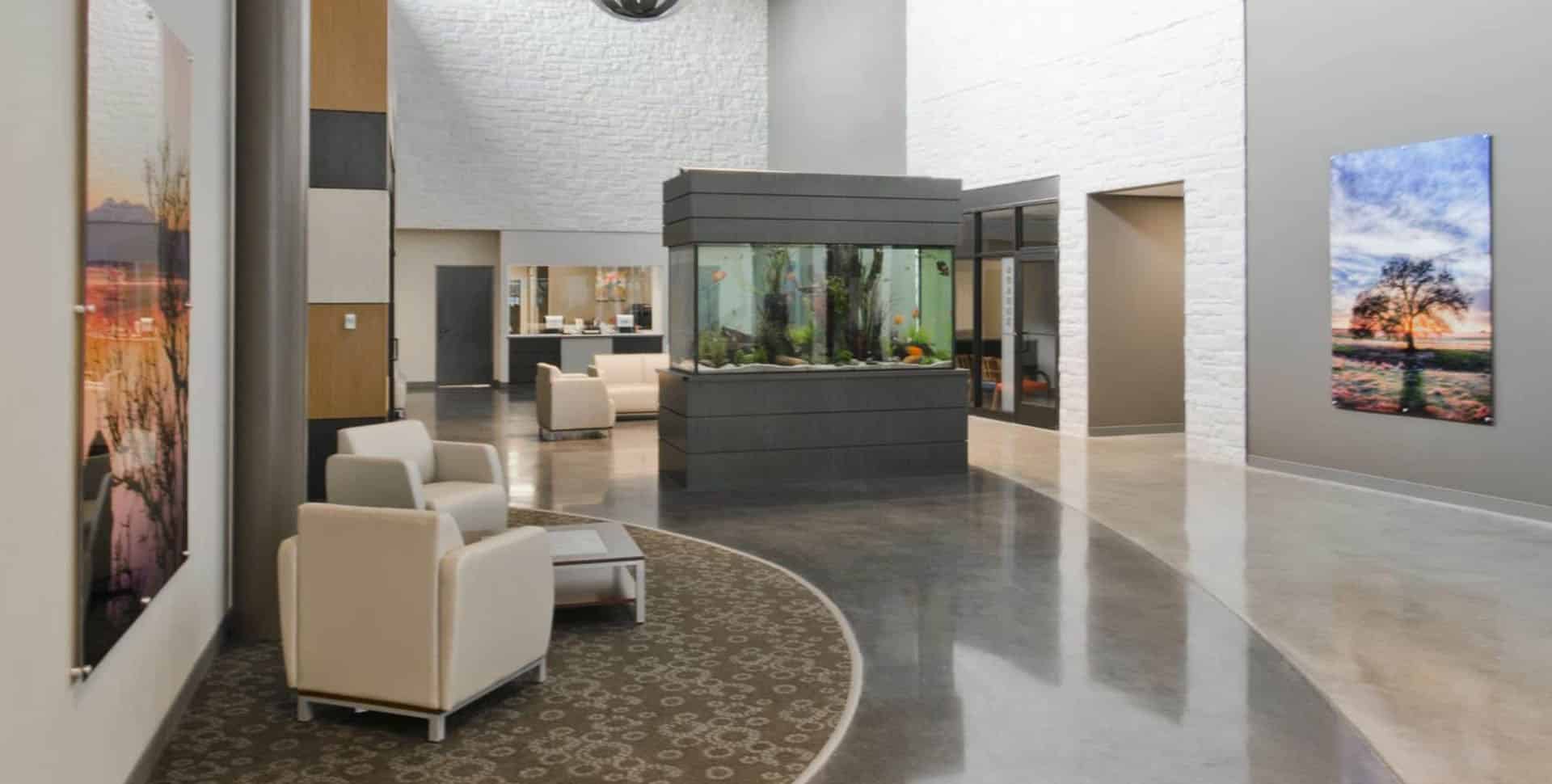 Modern lobby with white armchairs, a central fish tank, large landscape paintings on the walls, and a polished concrete floor.