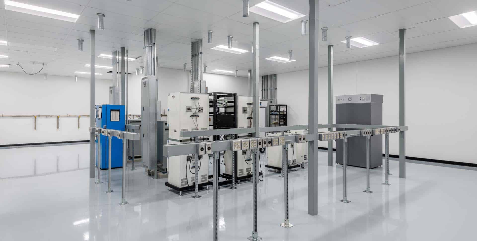 A clean, brightly lit room contains industrial electrical equipment, power distribution units, and metal poles with numerous outlets, reflecting a controlled technical environment.