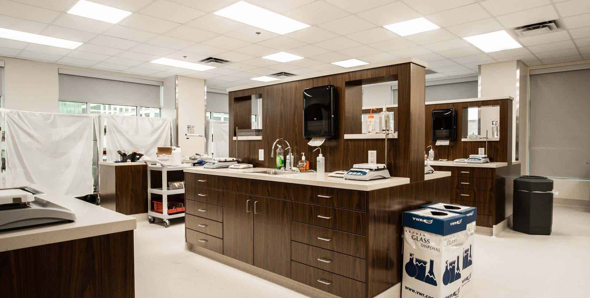 A modern medical clinic interior with wooden cabinetry, medical supplies, sinks, and equipment, divided by privacy curtains and bright overhead lighting.