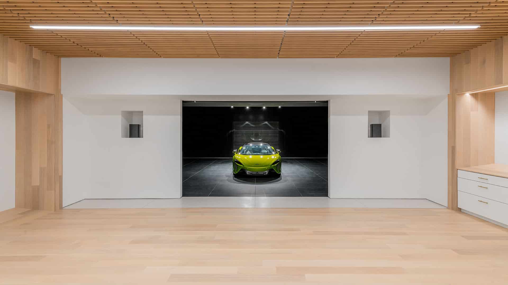 A bright green sports car is parked in a modern, minimalist garage with light wood floors, white walls, and a wooden slat ceiling.