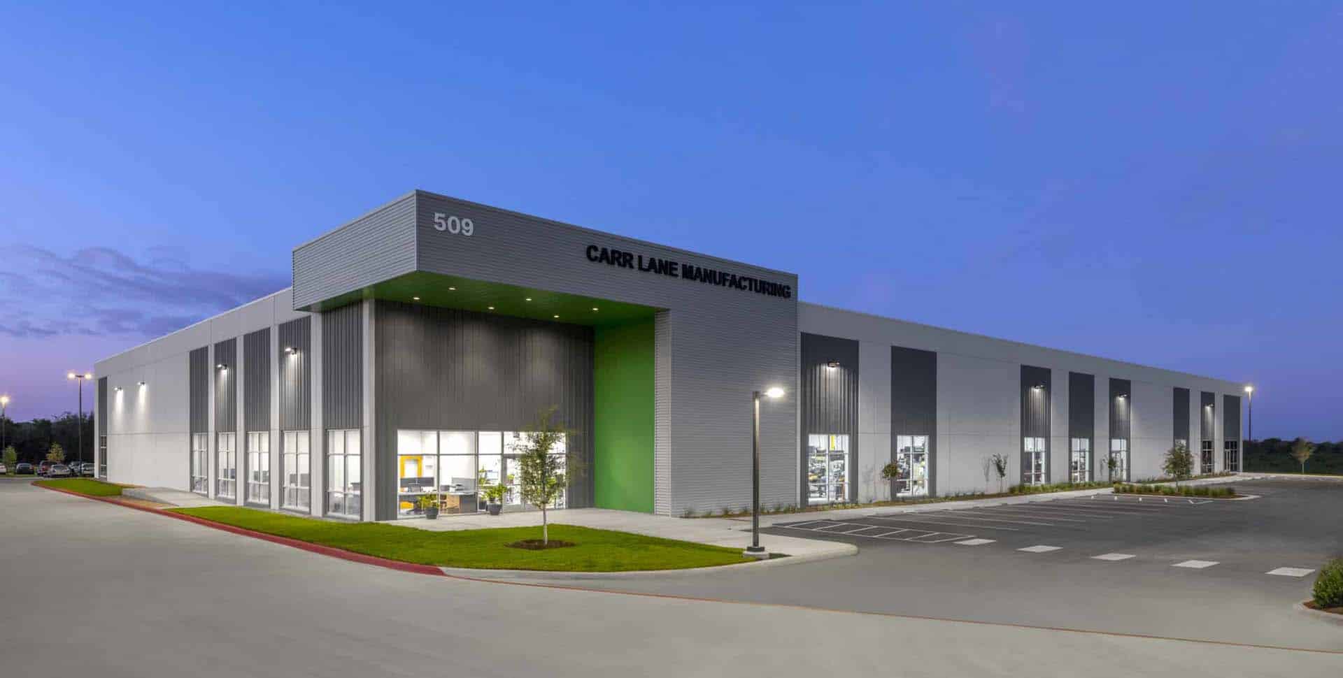 A modern industrial building labeled "Carr Lane Manufacturing" with large windows and a green accent, located at 509, photographed at dusk.