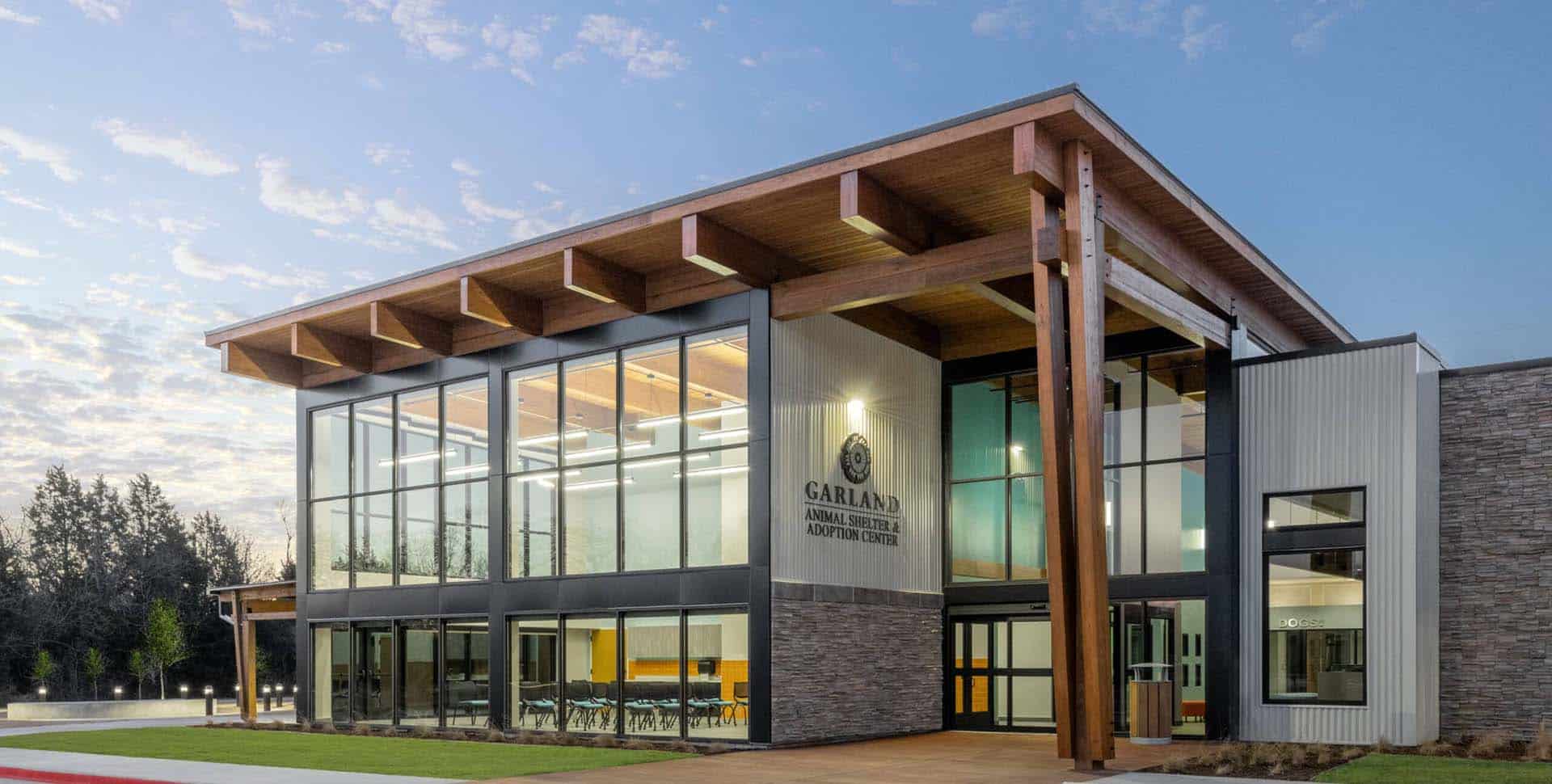 Modern two-story building with large glass windows and wood accents, labeled "Garland Animal Shelter & Adoption Center," set against a partly cloudy sky.