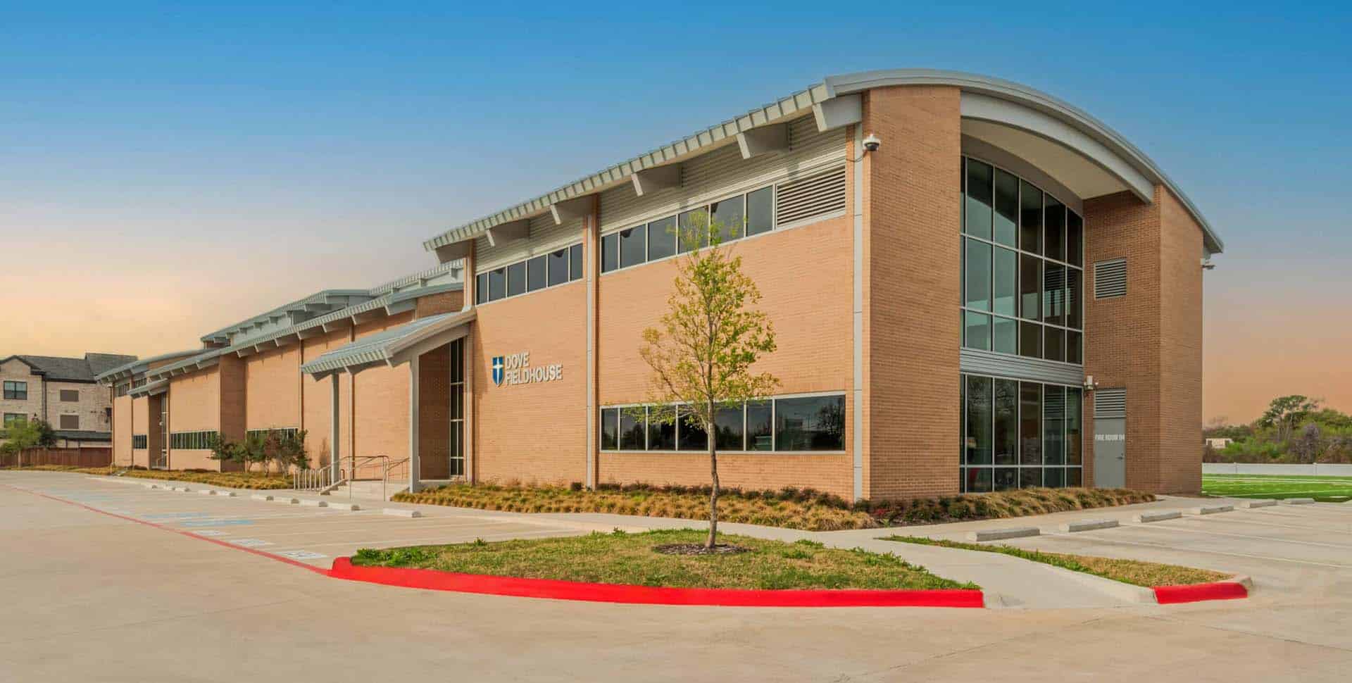 Two-story brick commercial building with large windows, an arched roof, and a small landscaped area in front; parking spaces are visible, some marked for accessibility.