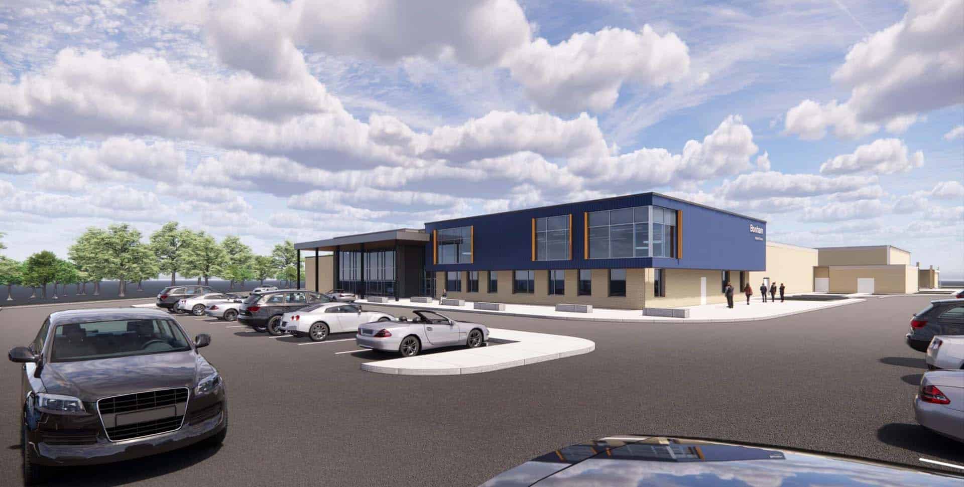 A modern two-story building with a blue façade and large windows, surrounded by a parking lot with several cars and a few people walking nearby under a partly cloudy sky.