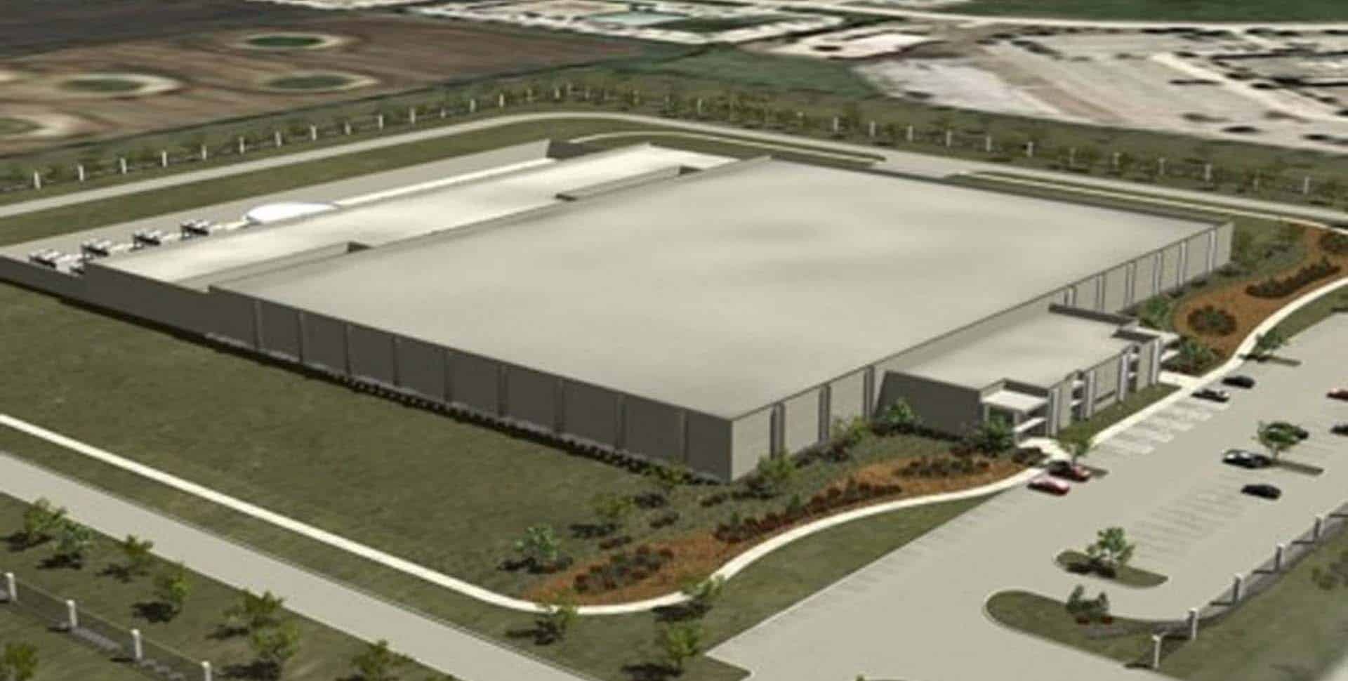 A large, rectangular industrial building with a flat roof, surrounded by landscaped grounds and parking areas.