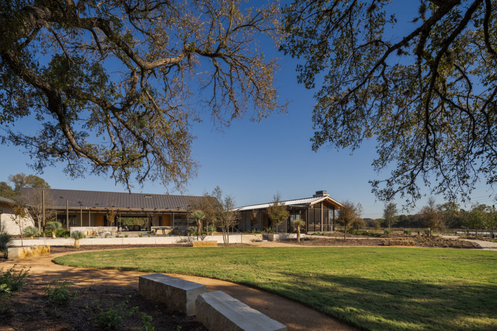 A view looking at the exterior of a building during the day, with trees overhead and green grass.