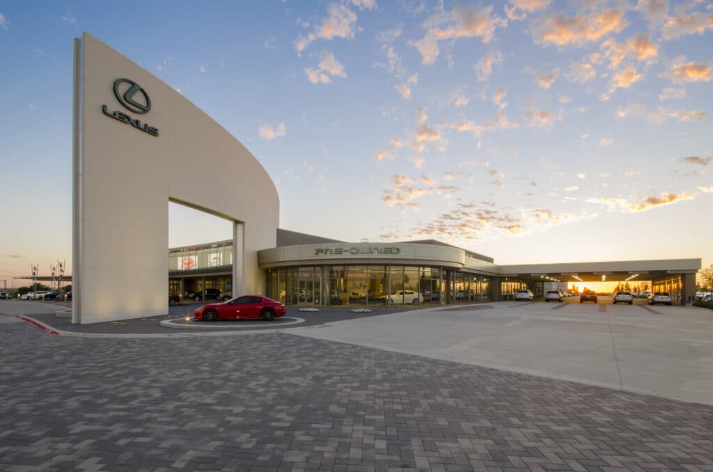 Image of the outside of a Lexus car dealership at sunset, with some cars sitting in front of the building.