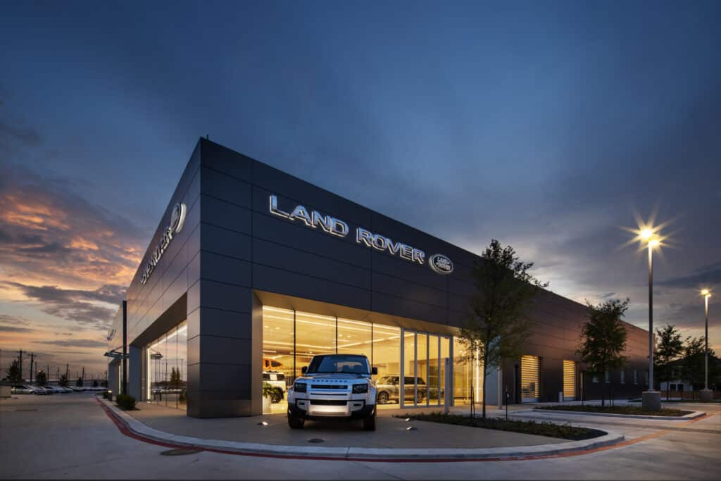 Photo of the exterior of a Land Rover car dealership at sunset, with a Land Rover vehicle parked in front of the corner of the building.