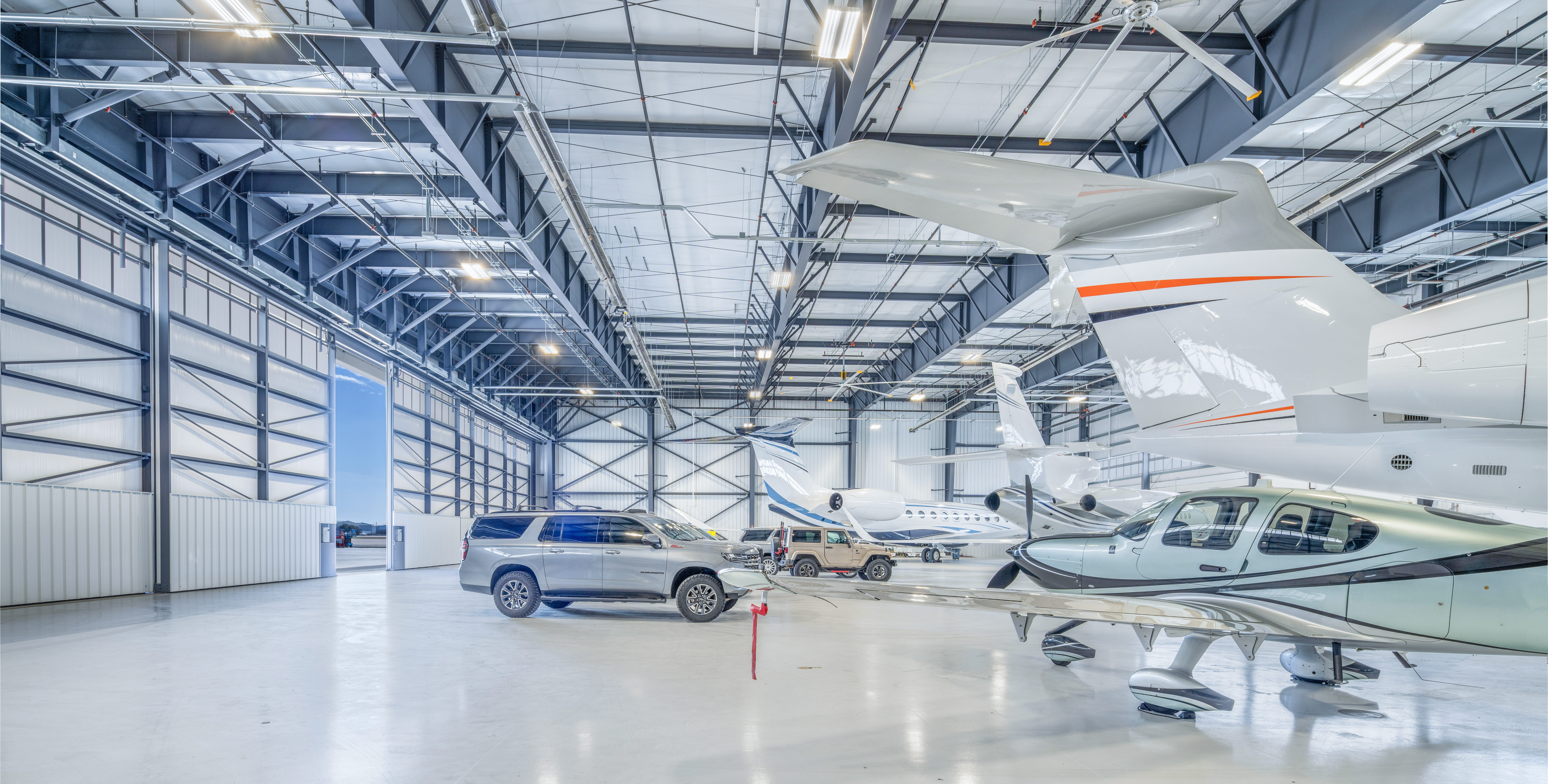 Inside of an airplane hangar with multiple small jet planes and vehicles spread throughout the inside of the hangar.