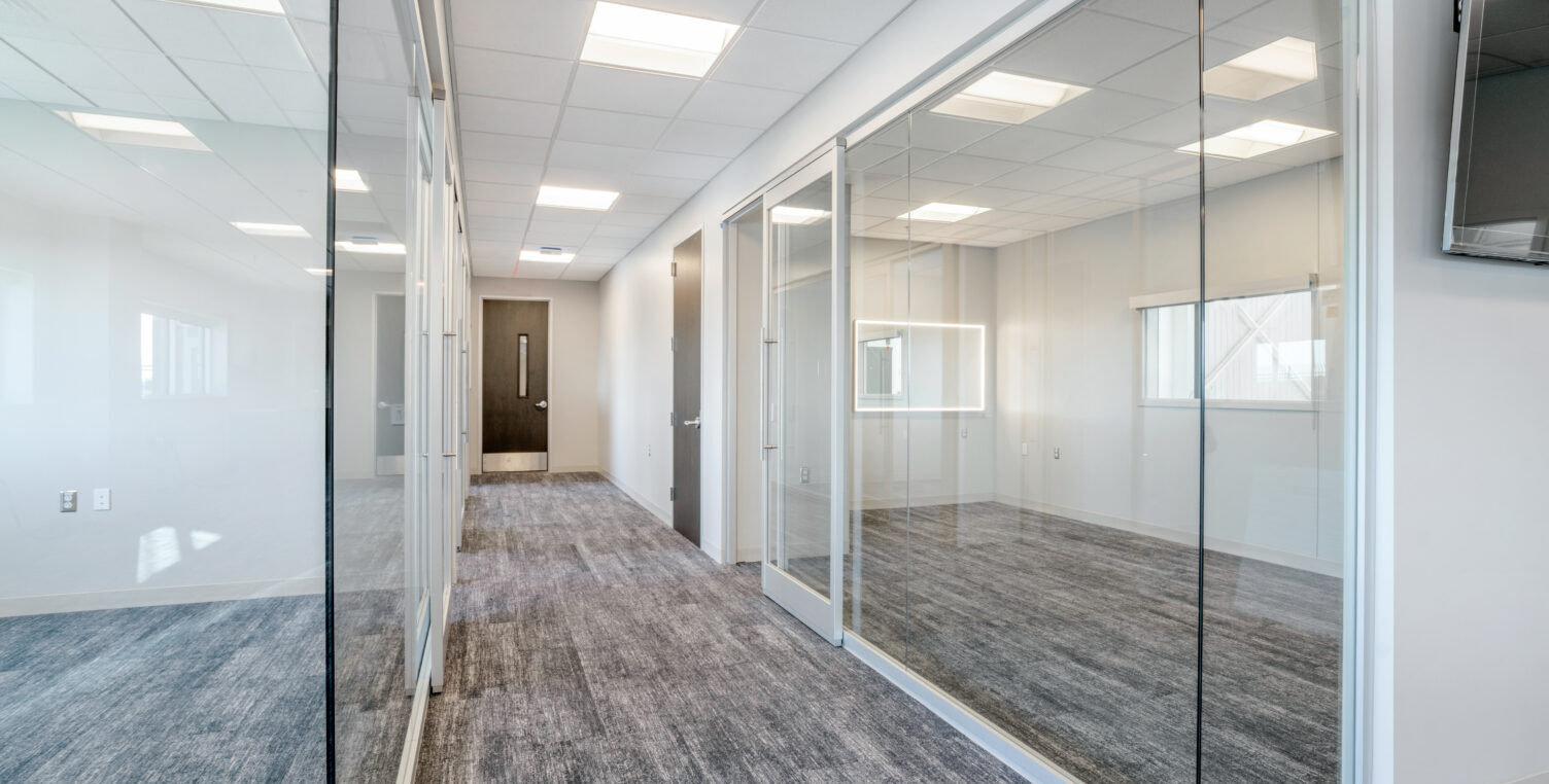 Interior of an empty office space looking down a hallway with a glassed-in conference room on the right
